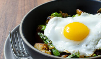 Bowl of potato hash with fava beans, green garlic, and a fried egg.