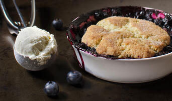Individual mixed berry cobbler topped with a buttermilk biscuit and scoop of ice cream.