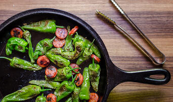 Blistered padron or shishito peppers with chorizo in a pan.