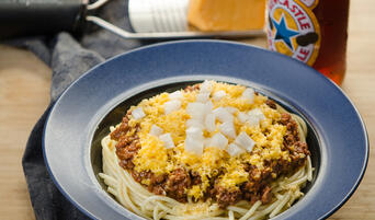 Bowl of Cincinnati Chili four ways with spaghetti, cheese, chili, and onions.