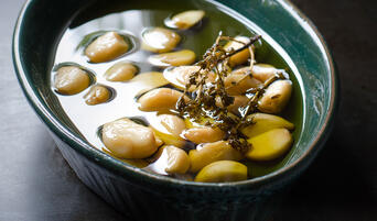 Cooked garlic confit in a dish with thyme and a bay leaf.
