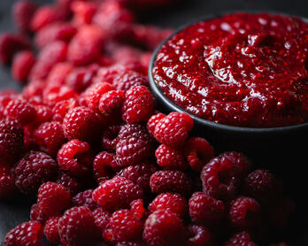 Bowl of raspberry jam alongside fresh raspberries.
